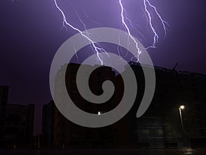 Lightning bolts light up sky in city during storm at night.