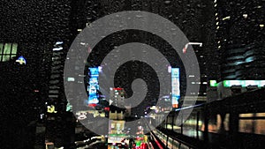 Lightning and rain in center of Bangkok with traffic, cars and train, at night, view through window with drops of rain