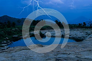 Lightning strikes over a dark forest with reflection on water