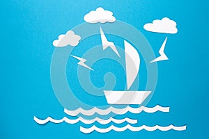 Lightning strikes in paper ship origami floats on waves. Clouds and lightning over white paper ship with sail on blue background