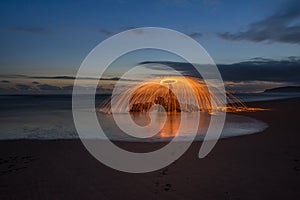 Lightpainted orb with flying sparks on a beach with a warm sunset in the background
