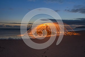 Lightpainted orb with flying sparks on a beach with a warm sunset in the background