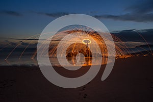 Lightpainted orb with flying sparks on a beach with a warm sunset in the background