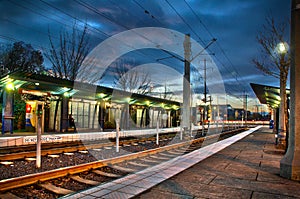 Lightrail station at sunset with rails and lights. Person on ben