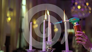 Lights candles with a gas burner. Candles are burning in candelabra candlestick.
