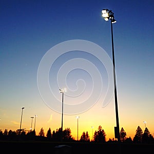 Lights coming on over sports fields at sunset.