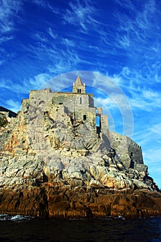 Liguria: the Saint Peter church of Portovenere on the cliff rockview and blue sky with clouds from the boat in the afternoon