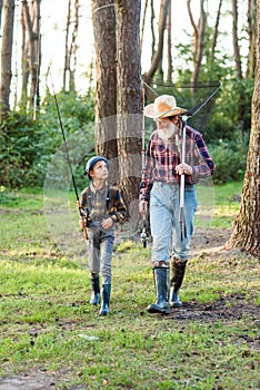 Likable confident bearded grandpa in forest going fishing together with his 10-aged grandson and talking about fishing. photo
