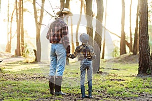 Likable confident bearded grandpa in forest going fishing together with his 10-aged grandson and talking about fishing.