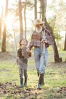 Likable confident bearded grandpa in forest going fishing together with his 10-aged grandson and talking about fishing.