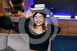 Likable joyful satisifed 25-aged woman putting on augmented reality goggles and working on virtual screen in the photo