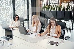 Likable young female office workers sitting at the meeting room and discussing their joint business project using photo