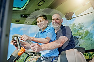 Like father, like son. Low angle portrait of a male farmer and his son inside the cockpit of a modern tractor.