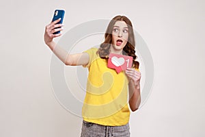 Like and follow my blog! Portrait of amazed blogger teen girl in yellow T-shirt holding social media