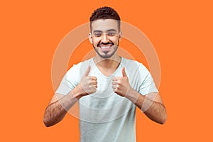 Like! Portrait of optimistic handsome brunette man showing thumbs up gesture. indoor studio shot isolated on orange background