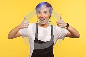 Like! Portrait of optimistic happy hipster woman showing double thumbs up and saying wow yes. yellow background, studio shot
