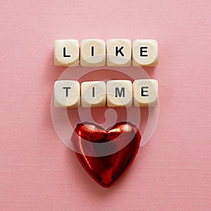 Like time words, made of wooden letters with red heart on pink background. Social media concept