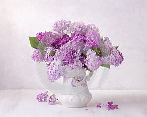 Lilac bouquet in the faience jug on a white wooden table. Soft focus photo