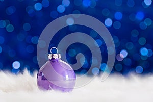 Lilac Christmas ball on white fur with garland lights on blue bo