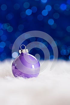 Lilac Christmas ball on white fur with garland lights on blue bo