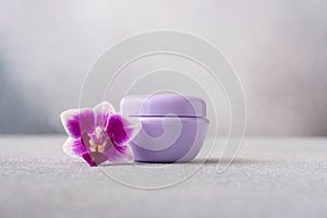 Lilac color cosmetic cream jar, product mockup on gray background with orchid flower