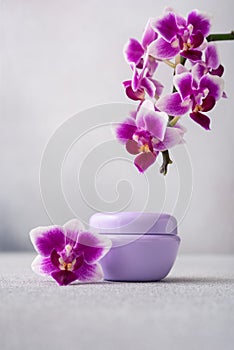 Lilac color cosmetic cream jar, product mockup on gray background with orchid flower