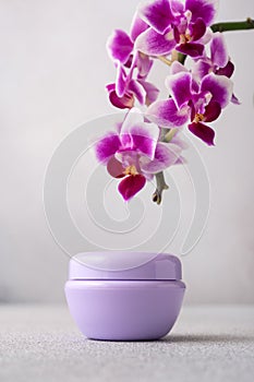 Lilac color cosmetic cream jar, product mockup on gray background with orchid flower