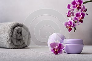 Lilac cosmetic cream jar and bath ball on gray background with orchid flower