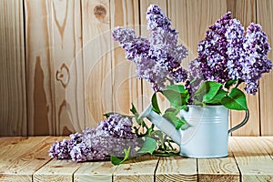 Lilac flovers in watering can on wood  background