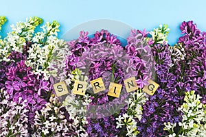 Lilac flower bloom background. Spring wooden lettres tex on blue background. Closeup blossom border flat lay photo