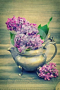 Lilac flowers in antique vase on wooden background. Vintage style