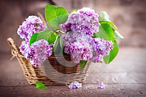 Lilac flowers bunch in a basket over blurred wood background