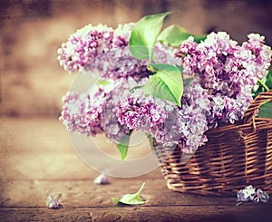 Lilac flowers bunch in a basket over blurred wood background