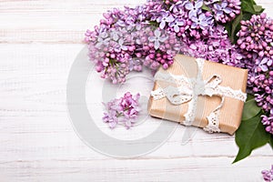 Lilac flowers and cute gift box on white wooden background,