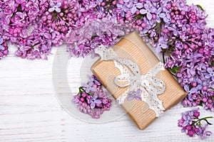 Lilac flowers and cute gift box on white wooden background, copy space.