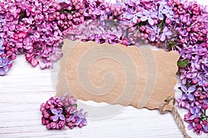 Lilac flowers and empyt card on white wooden background,