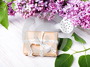 Lilac flowers and gift box on white wooden background