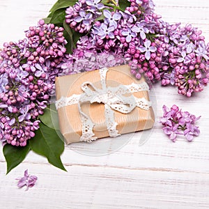 Lilac flowers and gift box on white wooden background,