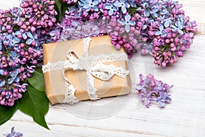 Lilac flowers and gift box on white wooden background