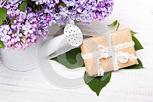 Lilac flowers and gift box on white wooden background
