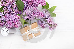 Lilac flowers and gift box on white wooden background