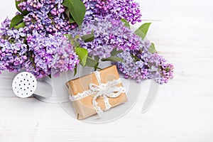 Lilac flowers and gift box on white wooden background