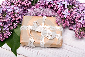 Lilac flowers and gift box on white wooden background