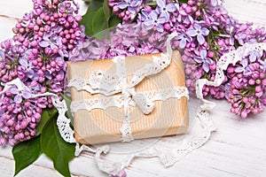 Lilac flowers and gift box on white wooden background