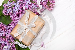 Lilac flowers and gift box on white wooden background,