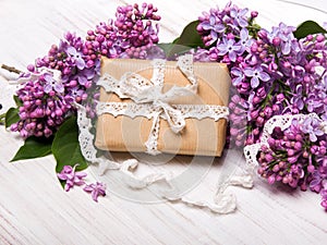 Lilac flowers, gift box on white wooden background