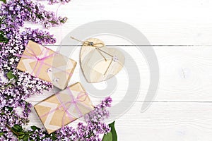 Lilac flowers with gift boxes and heart frame on white wooden background.