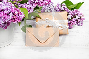 Lilac flowres, gift box and envelope on white wooden background.