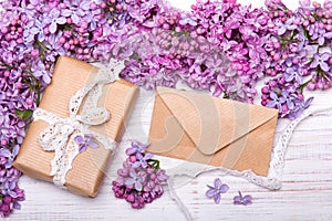 Lilac flowres, gift box and envelope on white wooden background.