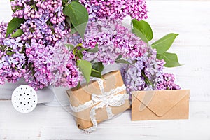 Lilac flowres, gift box and envelope on white wooden background.